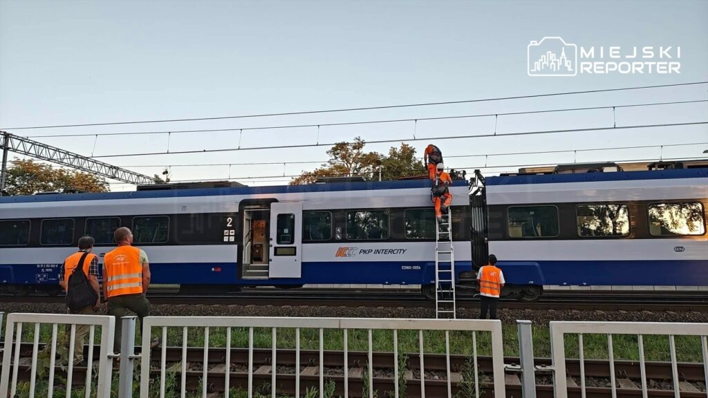 Grupa pracowników w pomarańczowych kamizelkach wykonuje prace konserwacyjne na dachu pociągu PKP Intercity.