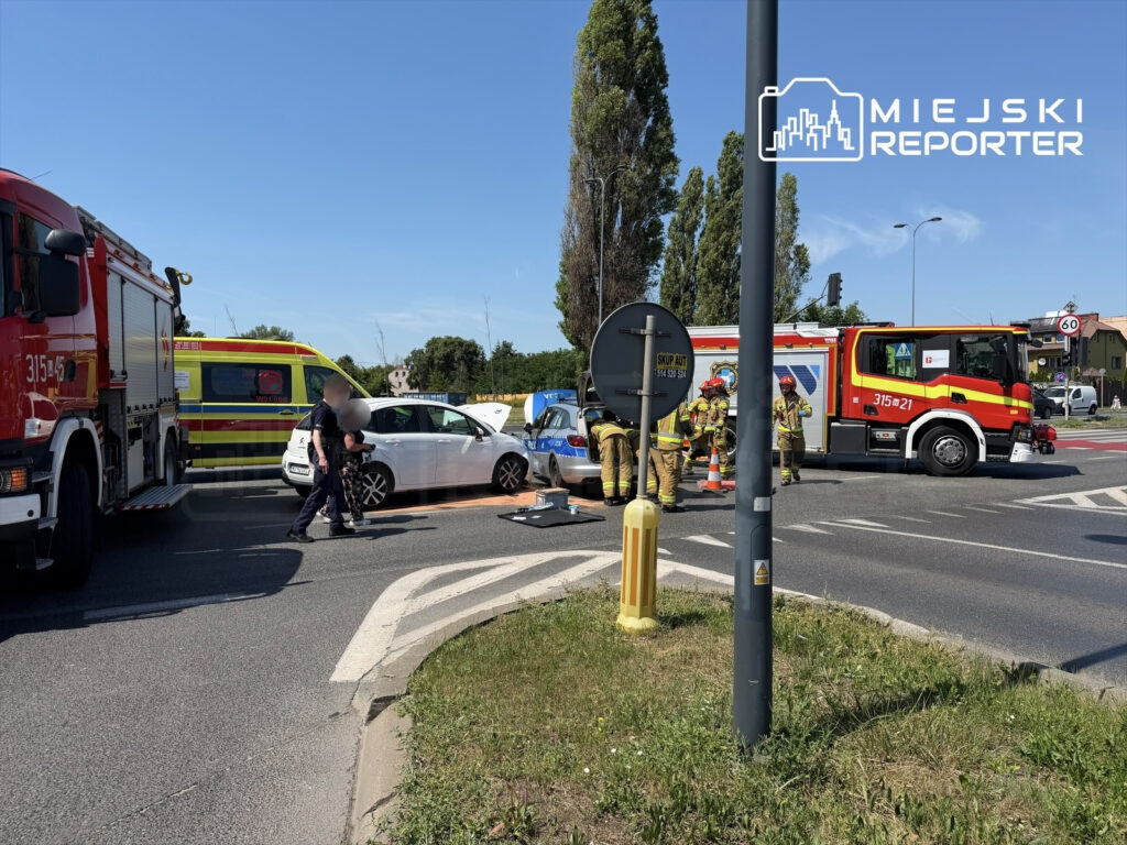 Na rondzie strażacy i policja udzielają pomocy poszkodowanym w wypadku drogowym, obok stoi wóz strażacki.