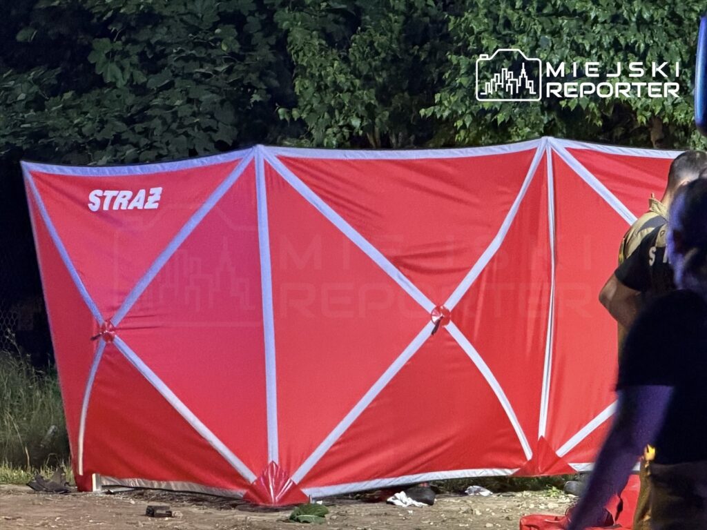Czerwony namiot z napisem "STRAŻ" ustawiony w zielonym otoczeniu, obok niego stoją osoby w mundurach.