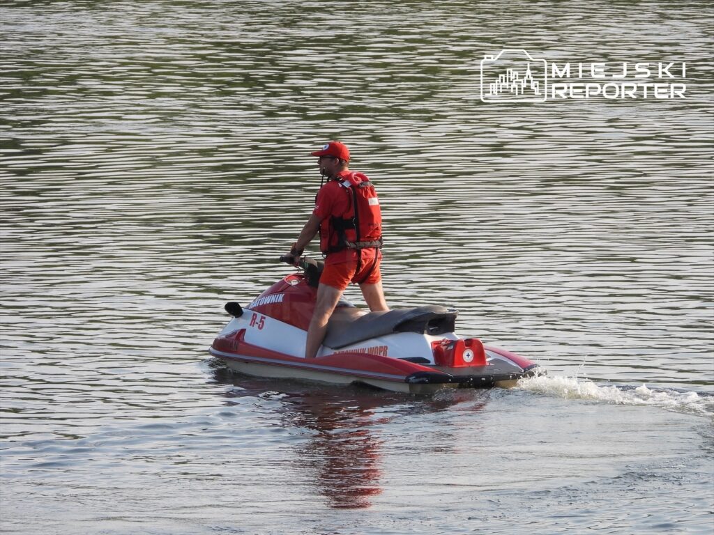 Ratownik na skuterze wodnym patroluje spokojną wodę jeziora w słoneczny dzień.