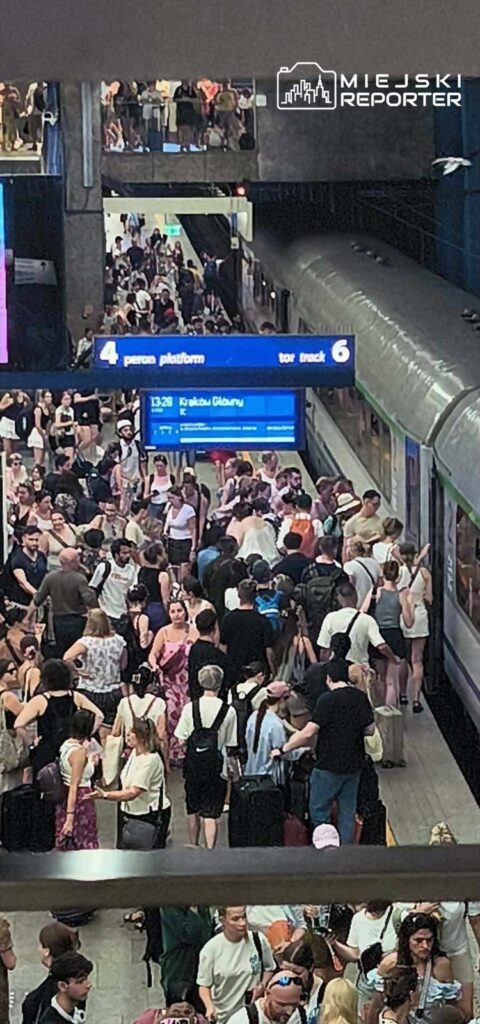Tłum ludzi czeka na peronie 4 na przyjazd pociągu, otoczeni tablicami informacyjnymi.