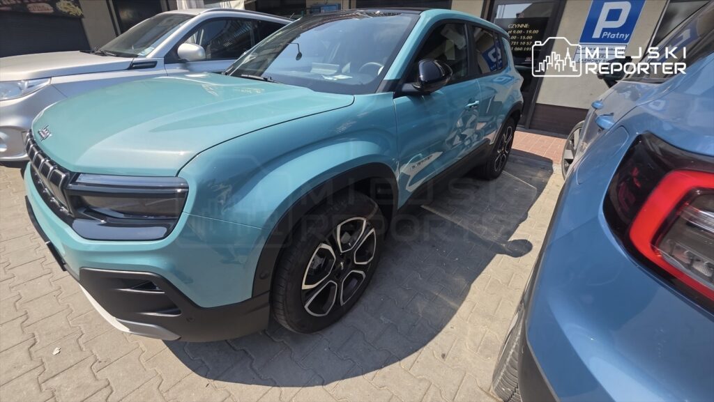 Nowoczesny SUV w kolorze turkusowym zaparkowany obok srebrnego pojazdu na utwardzonej nawierzchni.