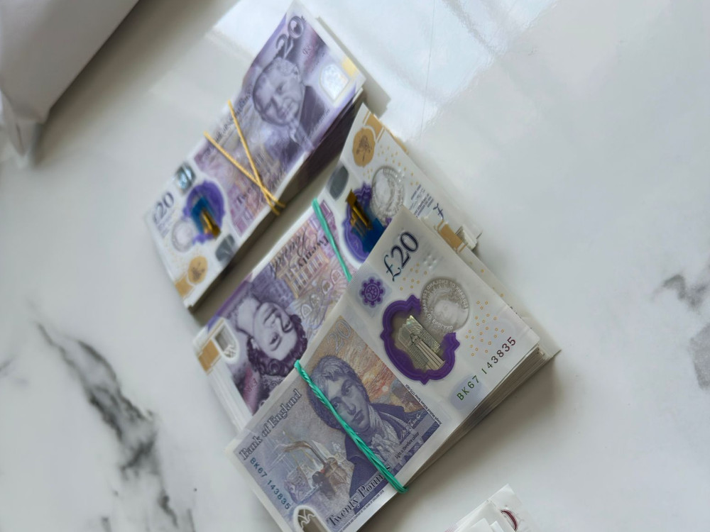Zestaw banknotów o nominale 20 funtów, związanych gumkami, leżący na marmurowym blacie.