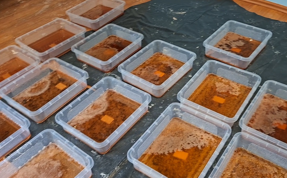 Plastikowe pojemniki z ciemnobrązową substancją rozmieszczone na podłodze w pomieszczeniu.