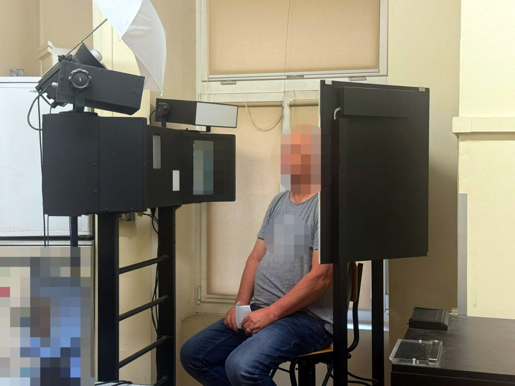 Mężczyzna siedzi na krześle przed urządzeniem do skanowania w pomieszczeniu biurowym.