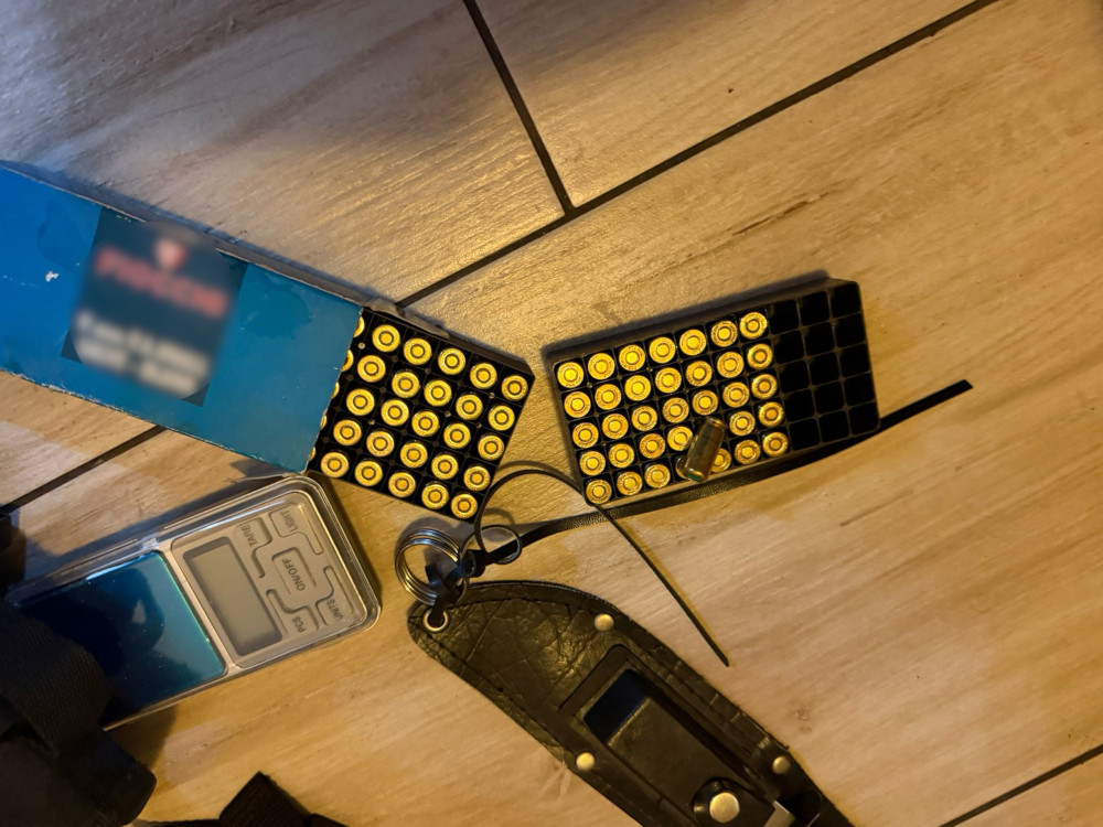 Na drewnianej podłodze leżą dwa magazynki z amunicją oraz elektroniczny urządzenie pomiarowe obok kluczy i opaski.