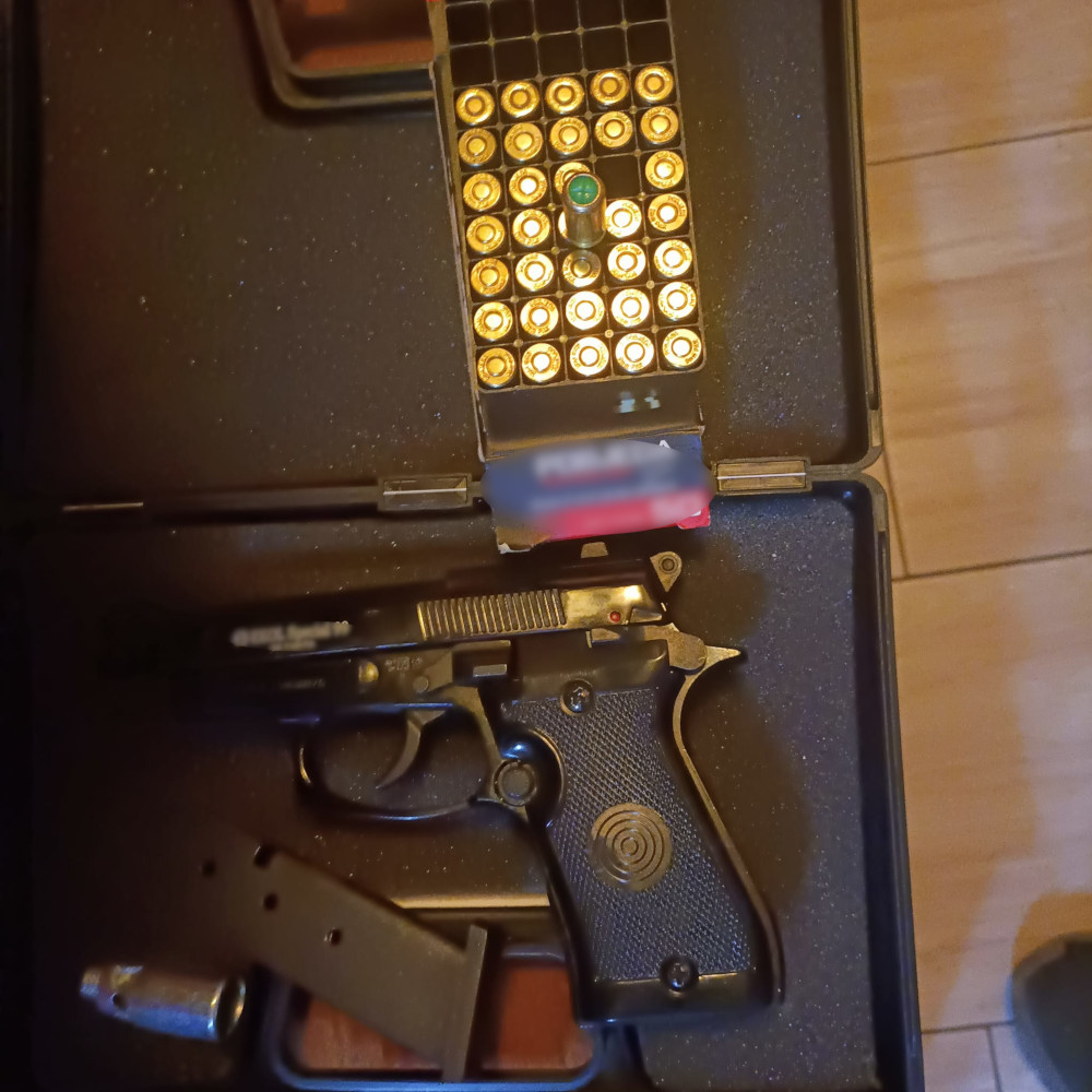 Pistolet leży obok magazynka z nabojami w czarnym futerale na tle podłogi.