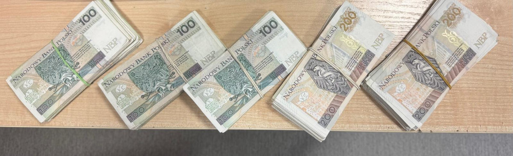 Stosy banknotów o nominale 100 i 200 złotych ułożone na drewnianym biurku.