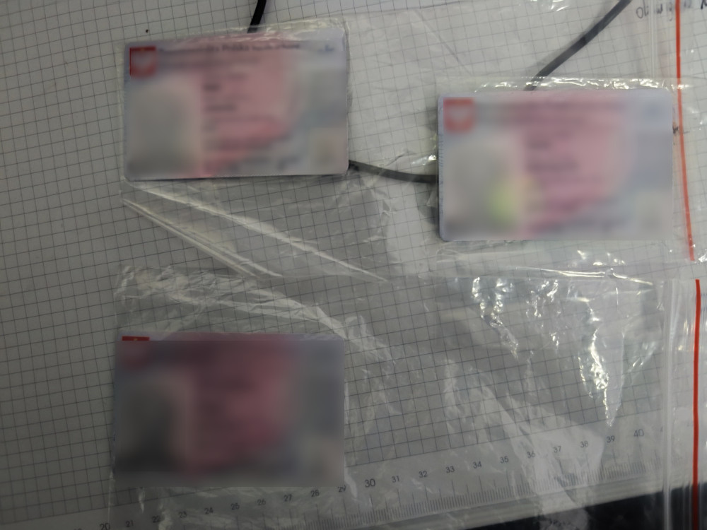 Trzy zablokowane dokumenty tożsamości umieszczone w przezroczystych kopertach na siatce papieru milimetrowego.