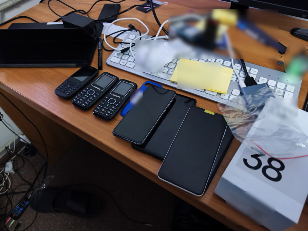 Na biurku leżą różne modele telefonów komórkowych, w tym klasyczne i nowoczesne smartfony, obok klawiatury komputerowej.