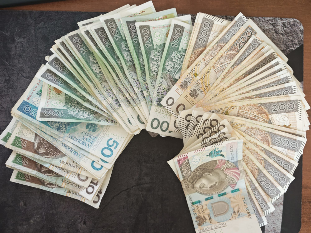 Stos banknotów o różnych nominałach ułożonych w półkole na ciemnym tle.