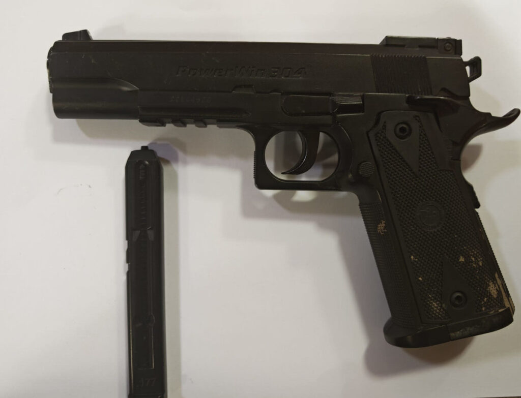 Pistolet w kolorze czarnym leży na białym tle obok magazynka.