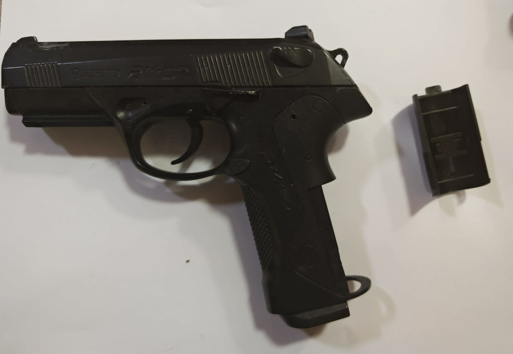 Pistolet w czarnym kolorze leżący na białym tle obok magazynka.