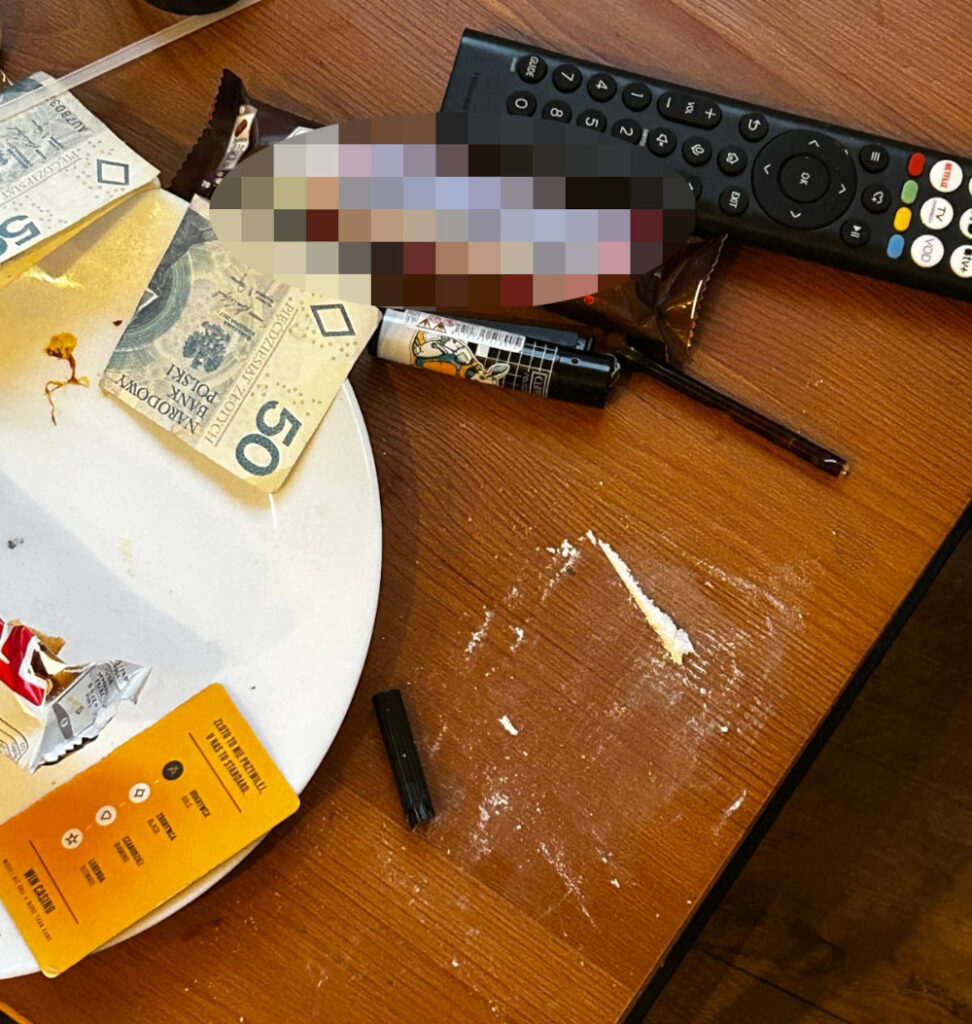 Na stole leżą banknoty, opakowania po słodyczach, a obok widoczna jest biała substancja oraz czarna długopis.