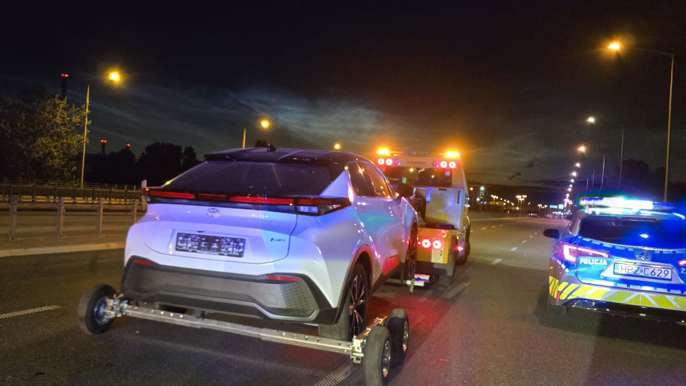 Toyota CHR holowana przez lawetę na oświetlonej ulicy nocą, obok policyjny radiowóz z włączonymi sygnałami.
