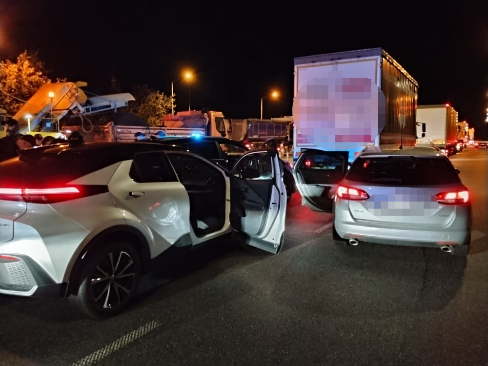 Policyjne samochody z otwartymi drzwiami zatrzymane na drodze, w tle ciężarówki i oświetlone miasto nocą.