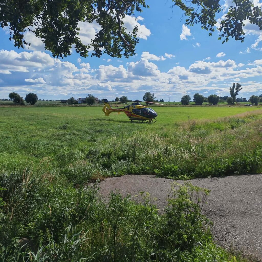 Lądowanie helikoptera ratunkowego na zielonej łące w słoneczny dzień, w tle chmury i drzewa.