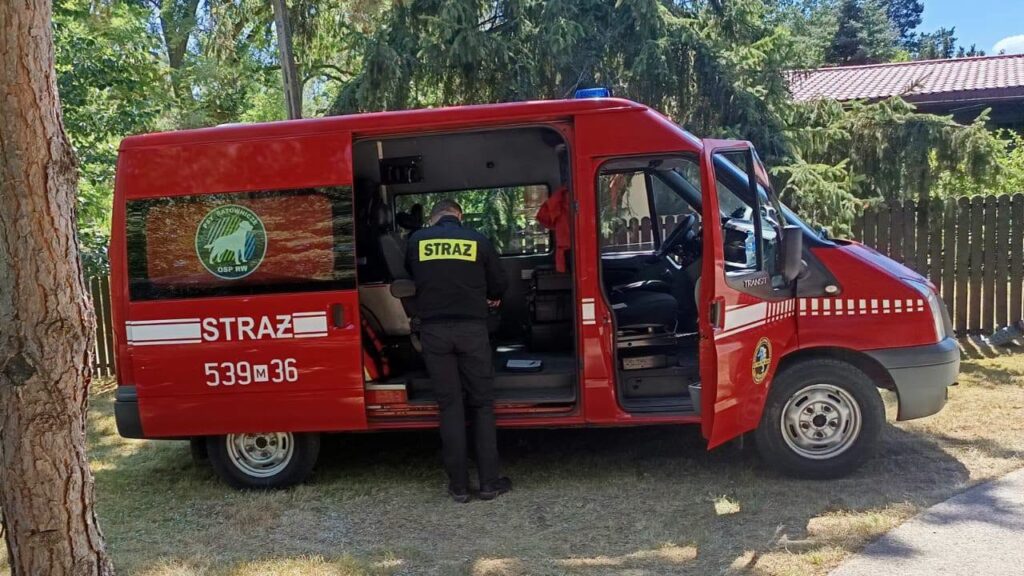 Ratownik w mundurze sprawdza wyposażenie w otwartym samochodzie ratunkowym na tle drzew.
