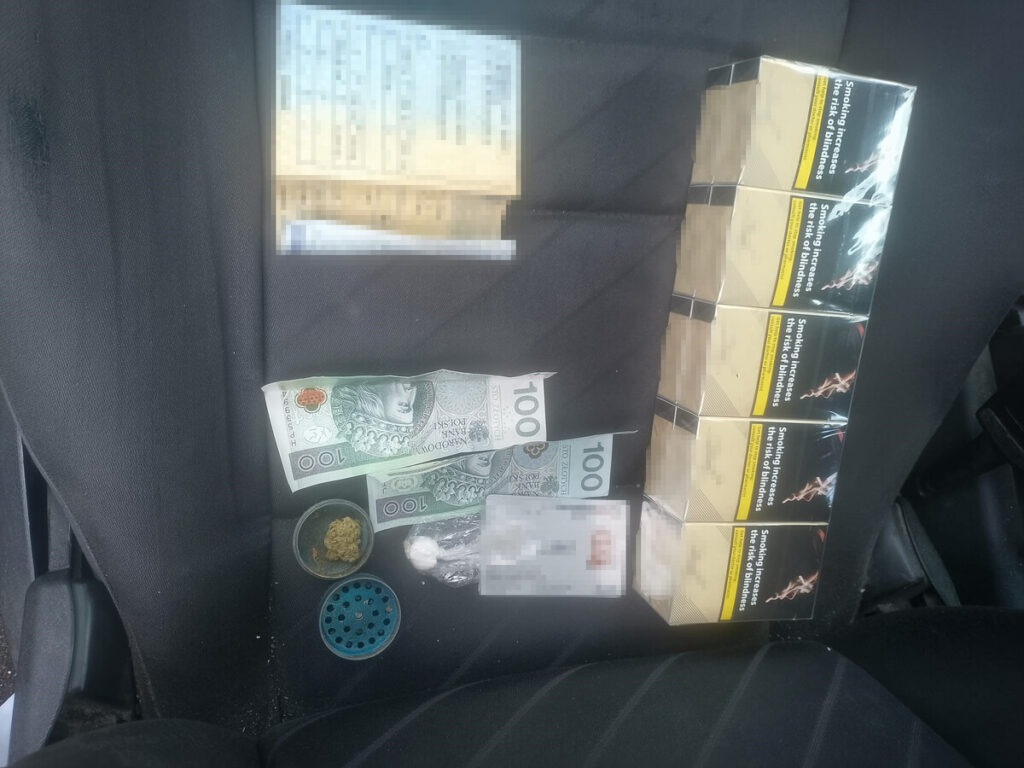 Na siedzeniu samochodu leżą paczki papierosów, banknoty oraz substancje w pojemnikach.