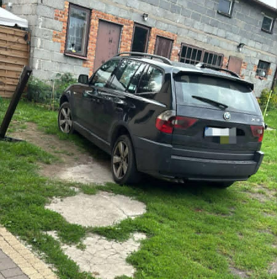 Czarny samochód SUV zaparkowany na trawie obok szarego budynku z oknami i drzwiami.