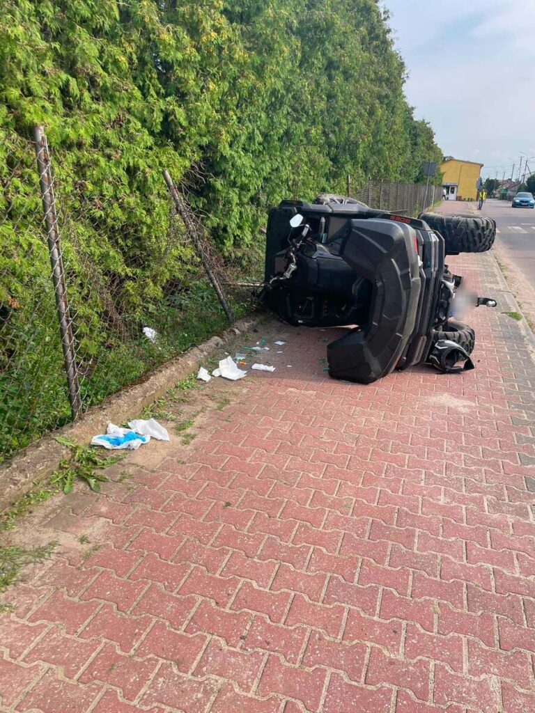 Na chodniku leży przewrócony quad obok gęstych krzewów, wokół porozrzucane śmieci.