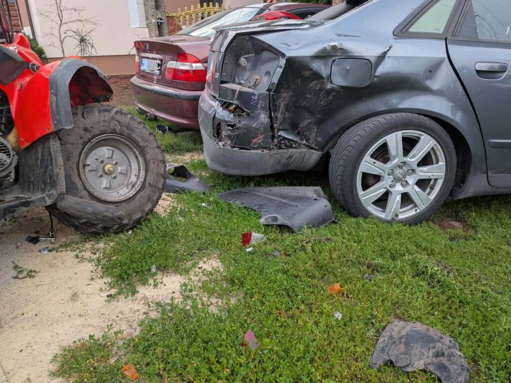 Czarny samochód osobowy z uszkodzoną tylną częścią stoi obok czerwonego quada na trawiastej przestrzeni.