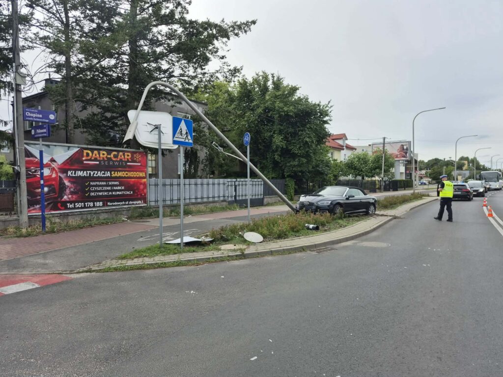 Policjant w kamizelce odblaskowej kieruje ruchem obok uszkodzonego słupa i samochodu na skrzyżowaniu.