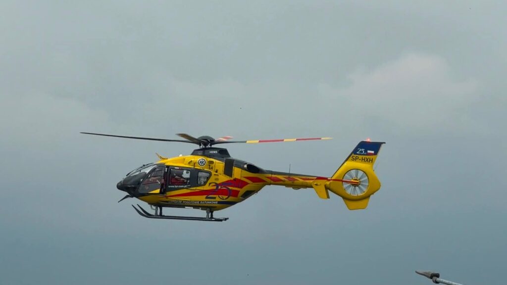 Żółty helikopter ratunkowy przelatuje nad szarym niebem.