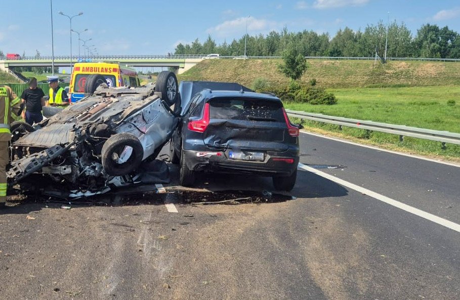 W wyniku wypadku drogowego na autostradzie leży przewrócone auto, obok stoi zespół ratunkowy.