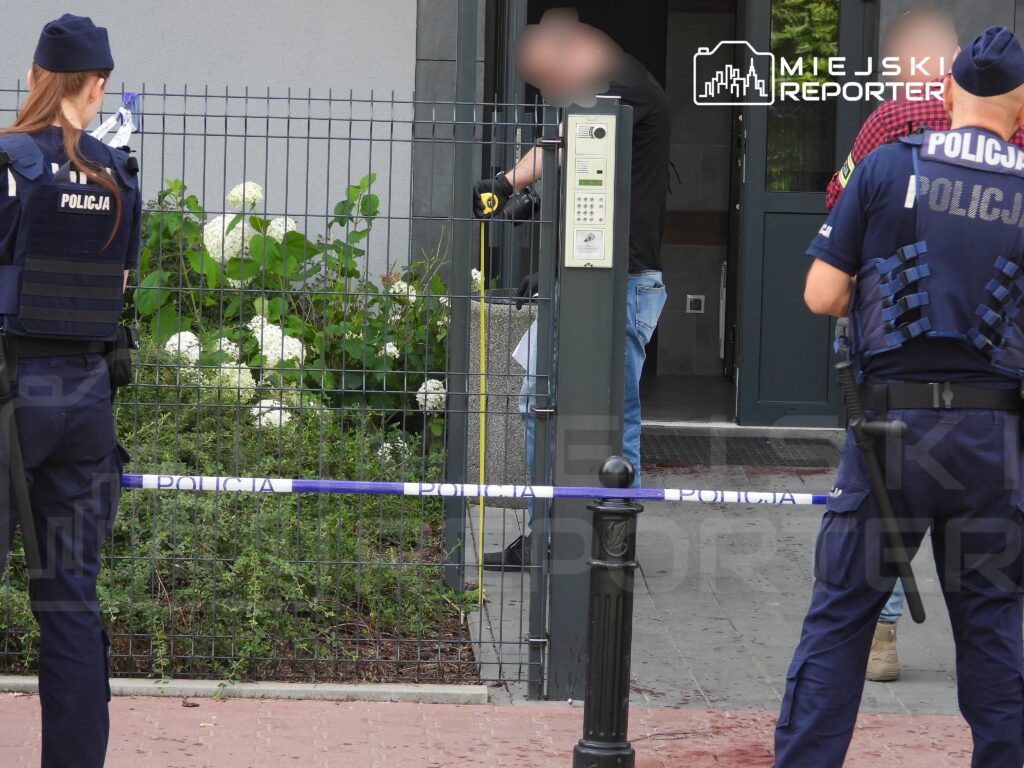 Policjanci zabezpieczają teren przed wejściem do budynku, gdzie prowadzone są czynności śledcze.