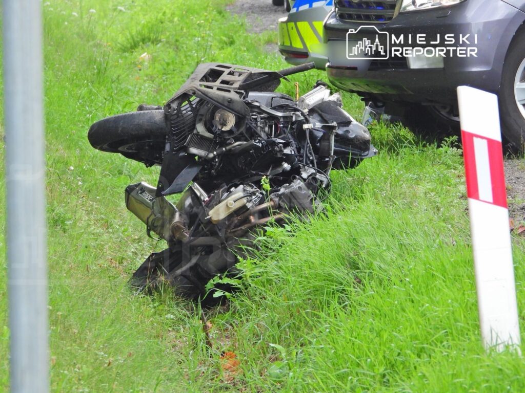 Zniszczony motocykl leży na trawie obok policyjnego samochodu.