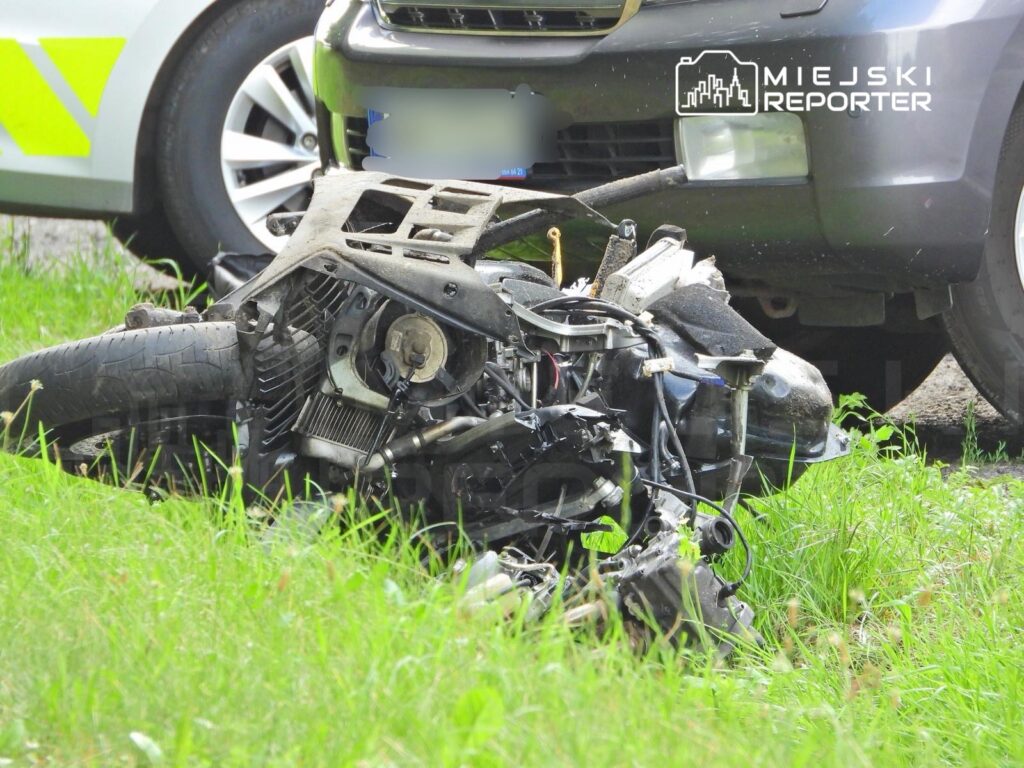 Zniszczony motocykl leży na poboczu drogi w pobliżu zaparkowanego samochodu.