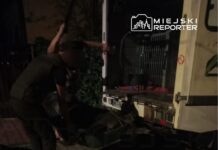 Dwóch mężczyzn w mundurach przenosi przedmiot do wnętrza pojazdu dostawczego w nocy na ulicy.