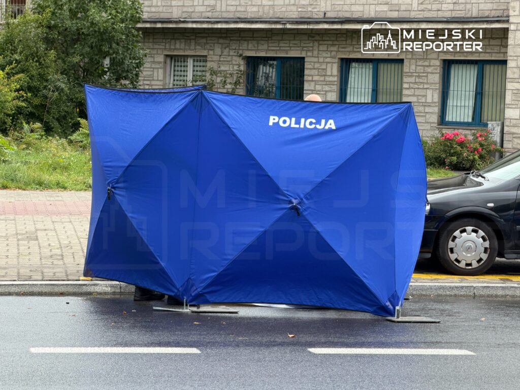Funkcjonariusze policji ustawiają niebieski namiot wzdłuż ulicy, obok zaparkowanego samochodu.