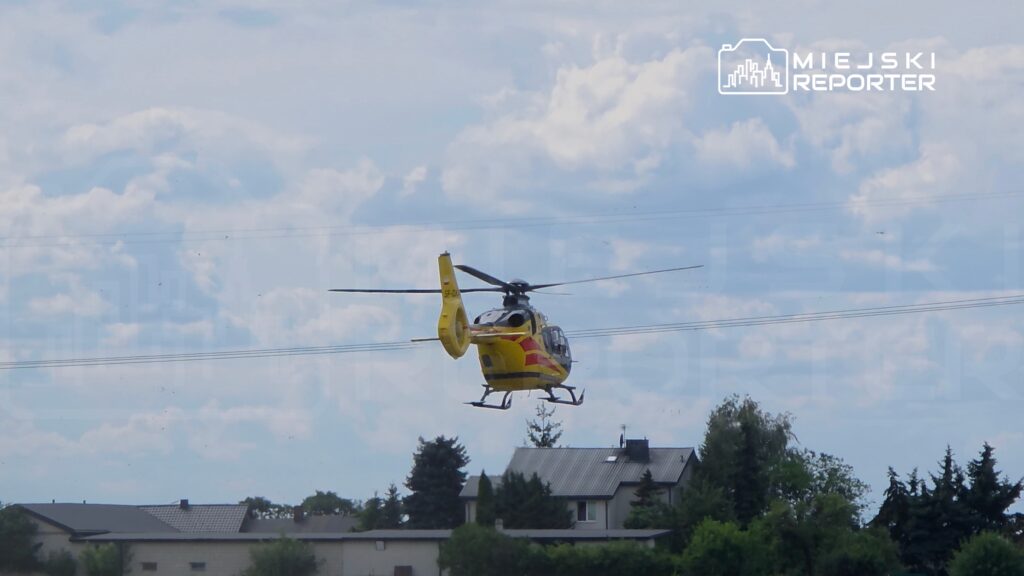 Śmigłowiec ratunkowy wylatuje z terenów zabudowanych w słoneczny dzień, na tle chmur.
