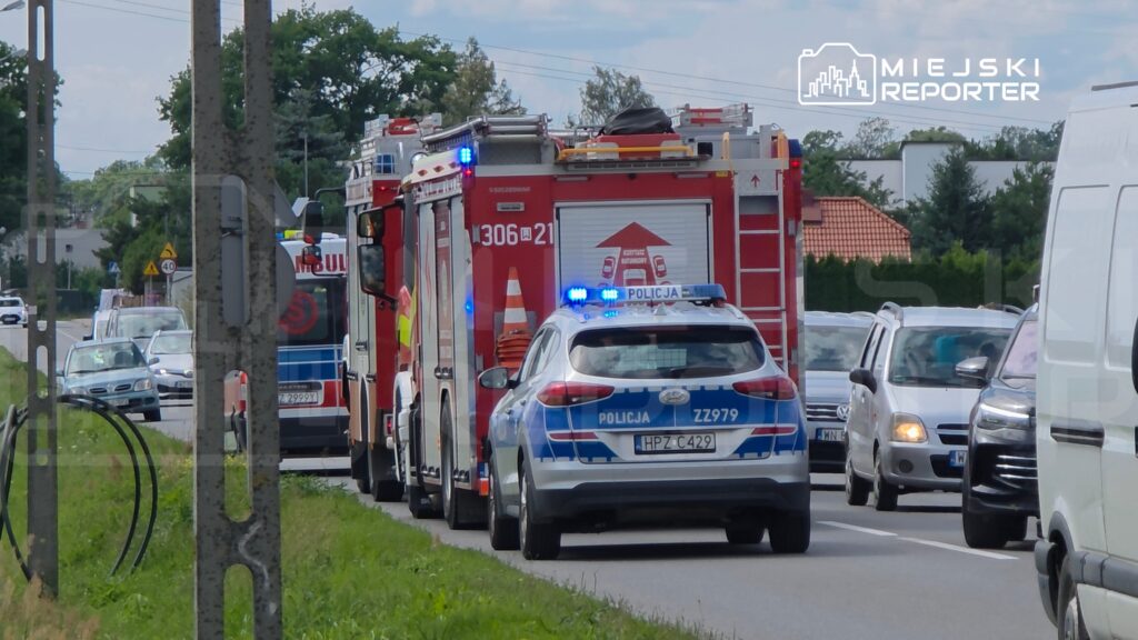 Karetka pogotowia oraz radiowóz policyjny zatrzymały się na drodze, obok nich widoczne są inne pojazdy.