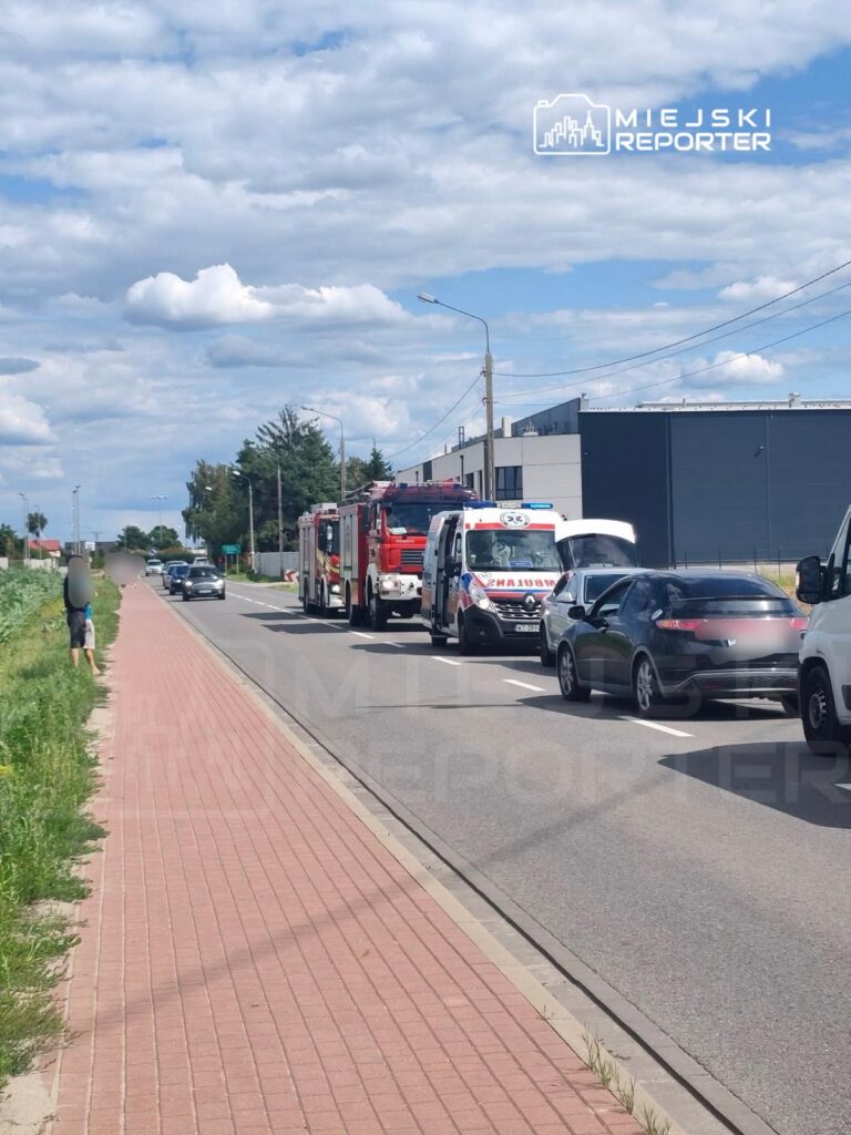 Na pasie drogi zatrzymały się pojazdy, w tym samochody strażackie i karetki, podczas gdy pieszy stoi na chodniku.
