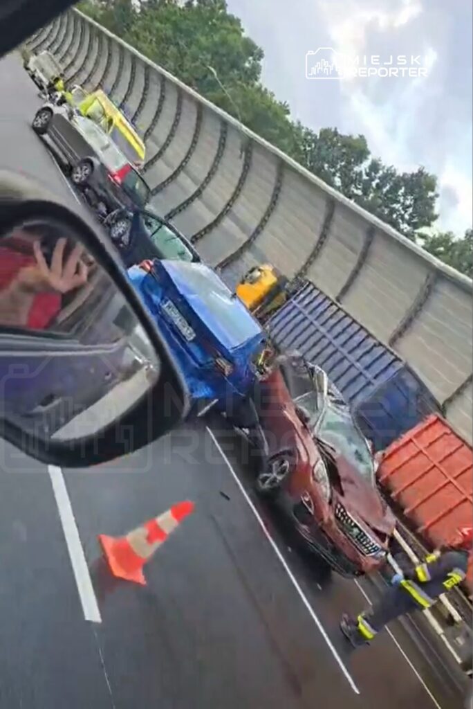 Wielokrotne zderzenie samochodów na drodze, obok pracujący strażak w mundurze, w tle kontenery.