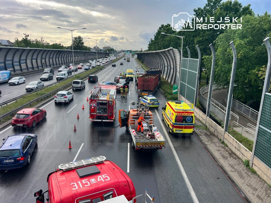 Na drodze znajduje się wypadek; strażacy i służby ratunkowe pracują przy uszkodzonych pojazdach.