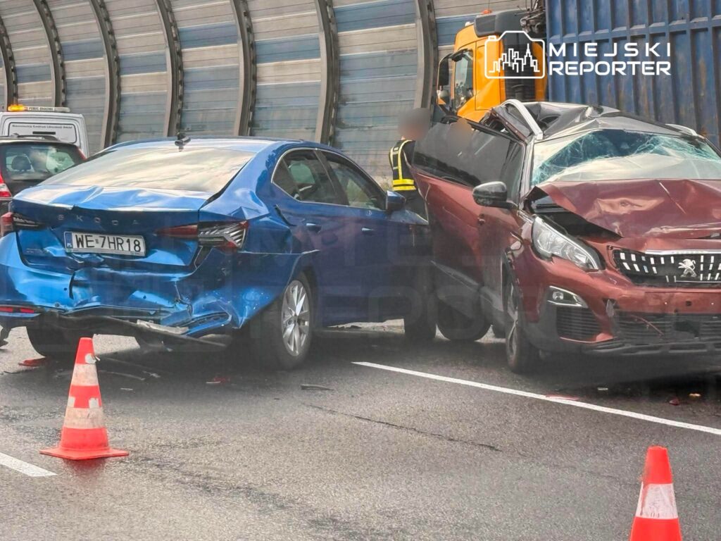 Zderzone samochody osobowe na drodze, z widocznymi uszkodzeniami i ustawionymi pachołkami drogowymi.