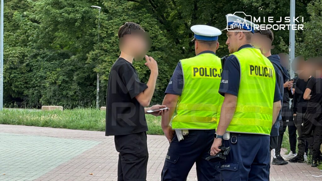 Młody mężczyzna rozmawia z dwoma policjantami w kamizelkach odblaskowych w parku.