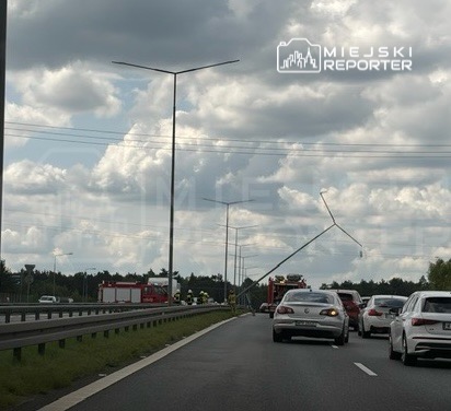 Złamany słup oświetleniowy leży na jezdni, obok stoją pojazdy oraz wozów strażackich.