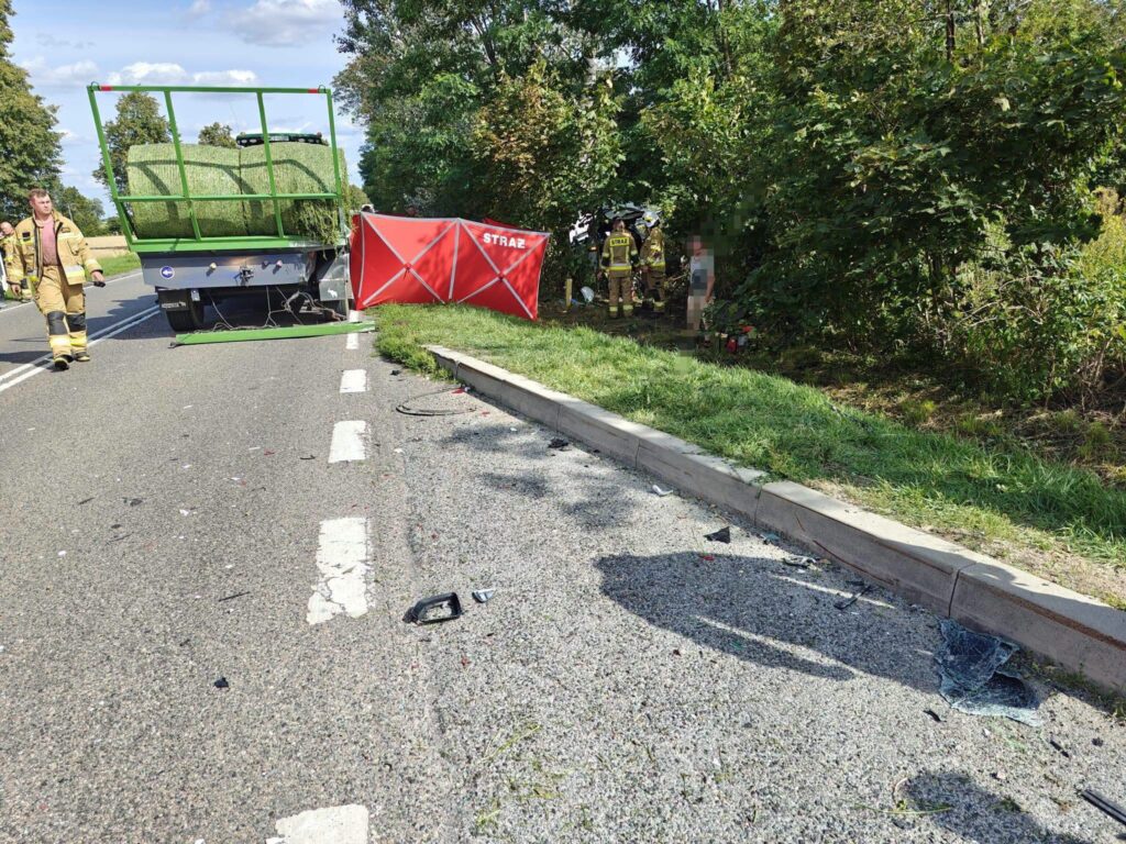Strażacy pracują przy wypadku drogowym obok przewróconej ciężarówki na poboczu drogi, z widocznymi odłamkami szkła.