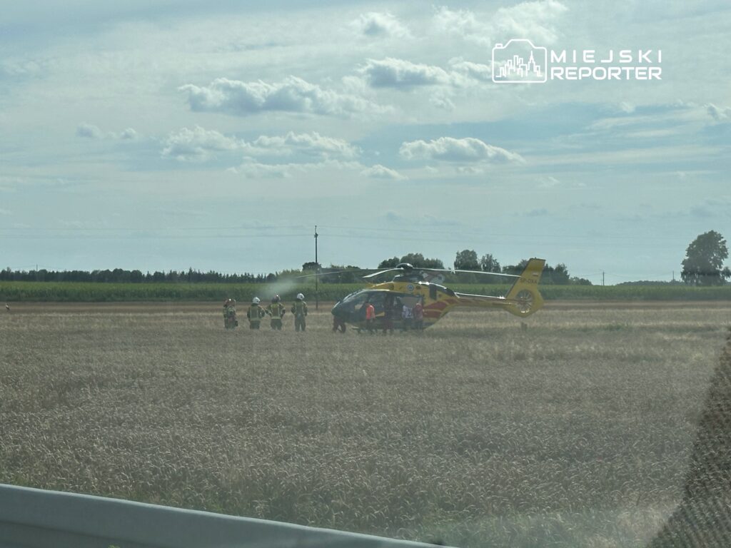 Zespół ratunkowy w odblaskowych kamizelkach gromadzi się wokół helikoptera na polu.