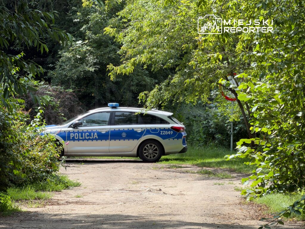 Radiowóz policji zaparkowany na leśnej drodze, otoczony gęstą roślinnością.