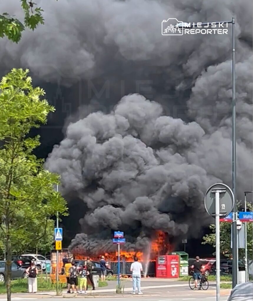 Wielka chmura czarnego dymu unosząca się nad płonącymi kontenerami na ulicy, w otoczeniu zdezorientowanych przechodniów.