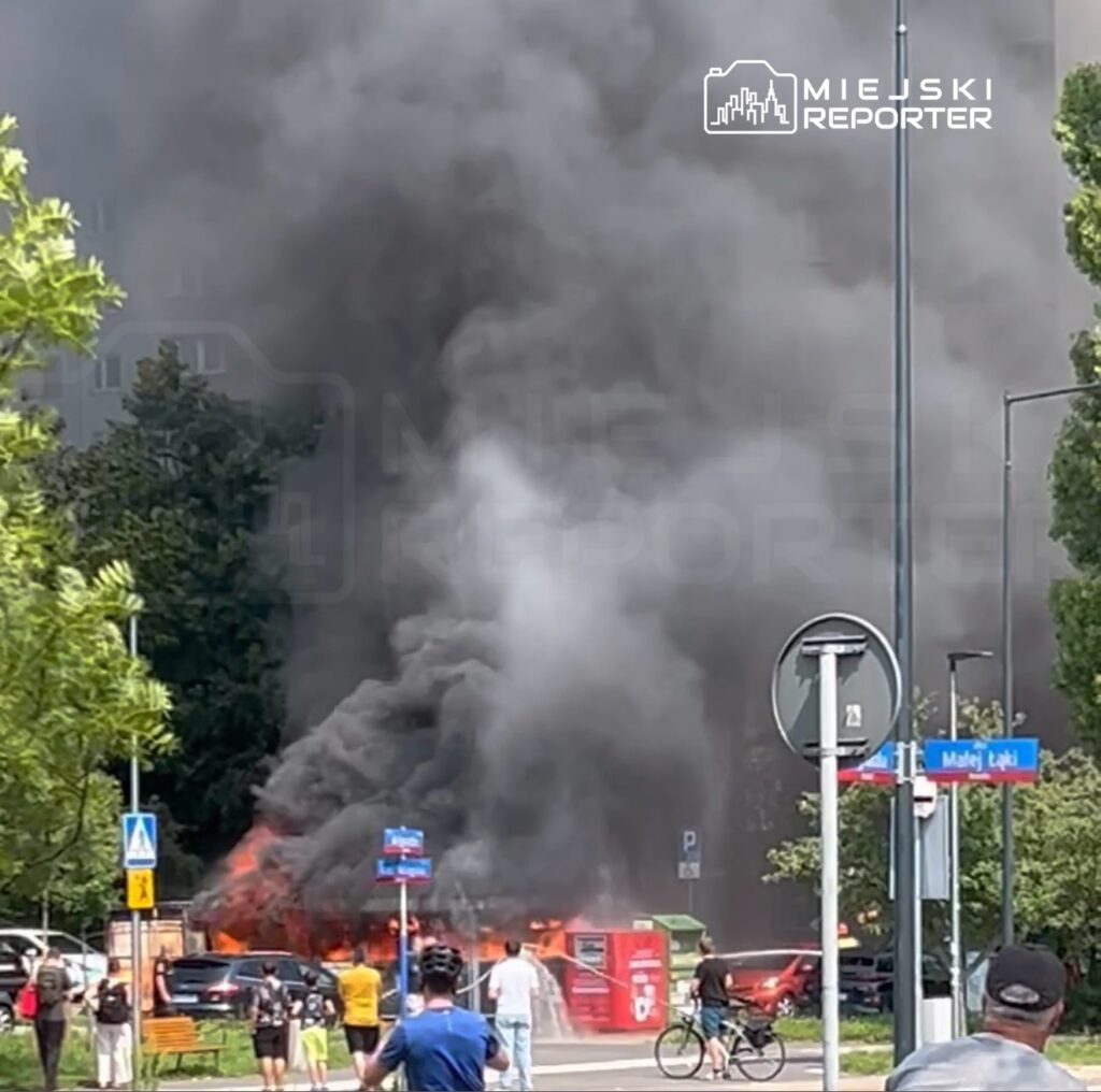 Wielka chmura czarnego dymu unosząca się z płonącego kontenera na śmieci w miejskim otoczeniu, wśród gapiów.