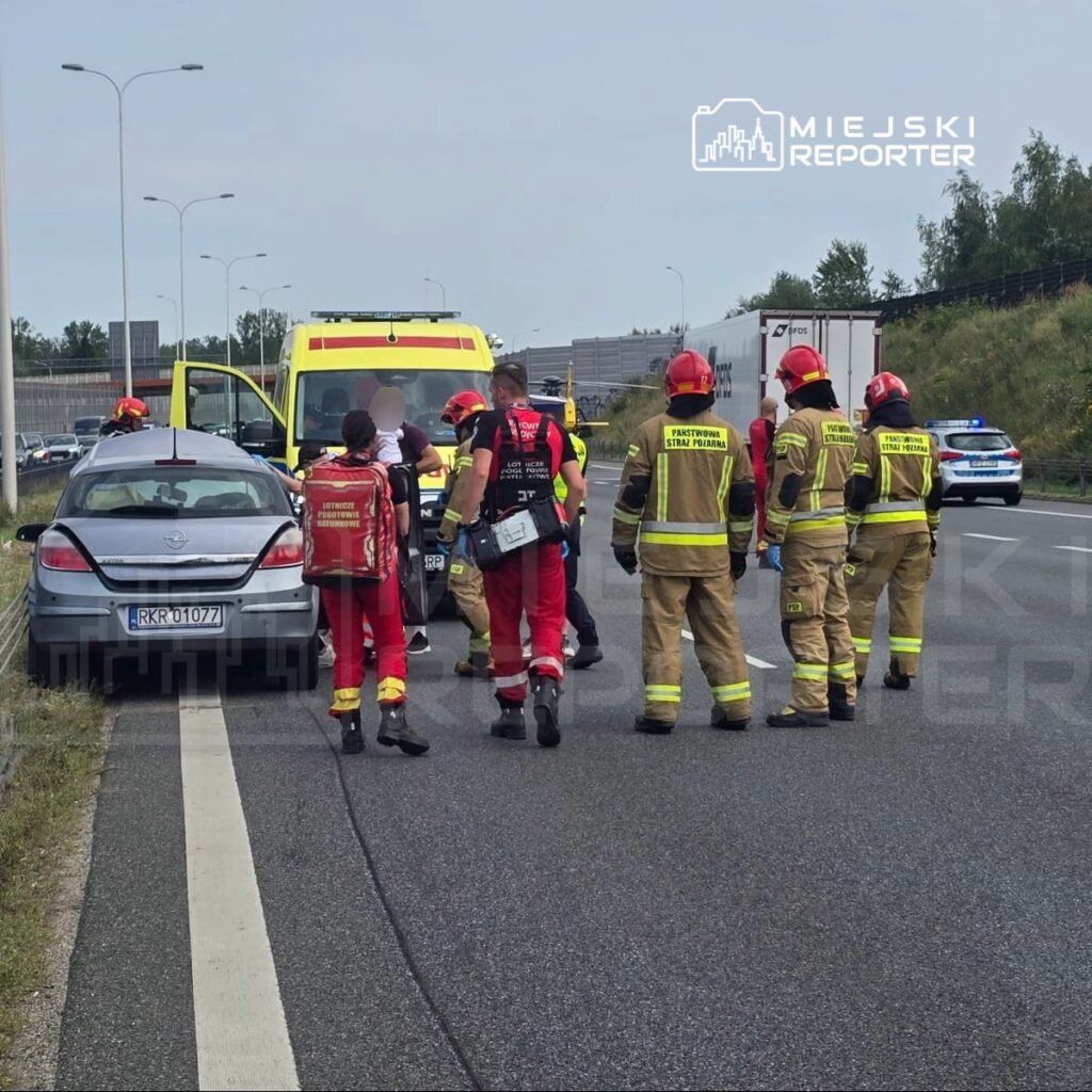 Grupa ratowników medycznych i strażaków udziela pomocy poszkodowanemu przy samochodzie na autostradzie.