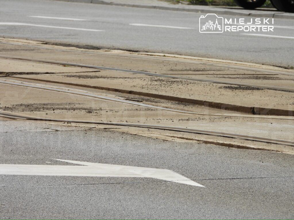 Zabytkowe torowisko tramwajowe widoczne na skrzyżowaniu z oznakowaniem drogowym w kierunku w lewo.