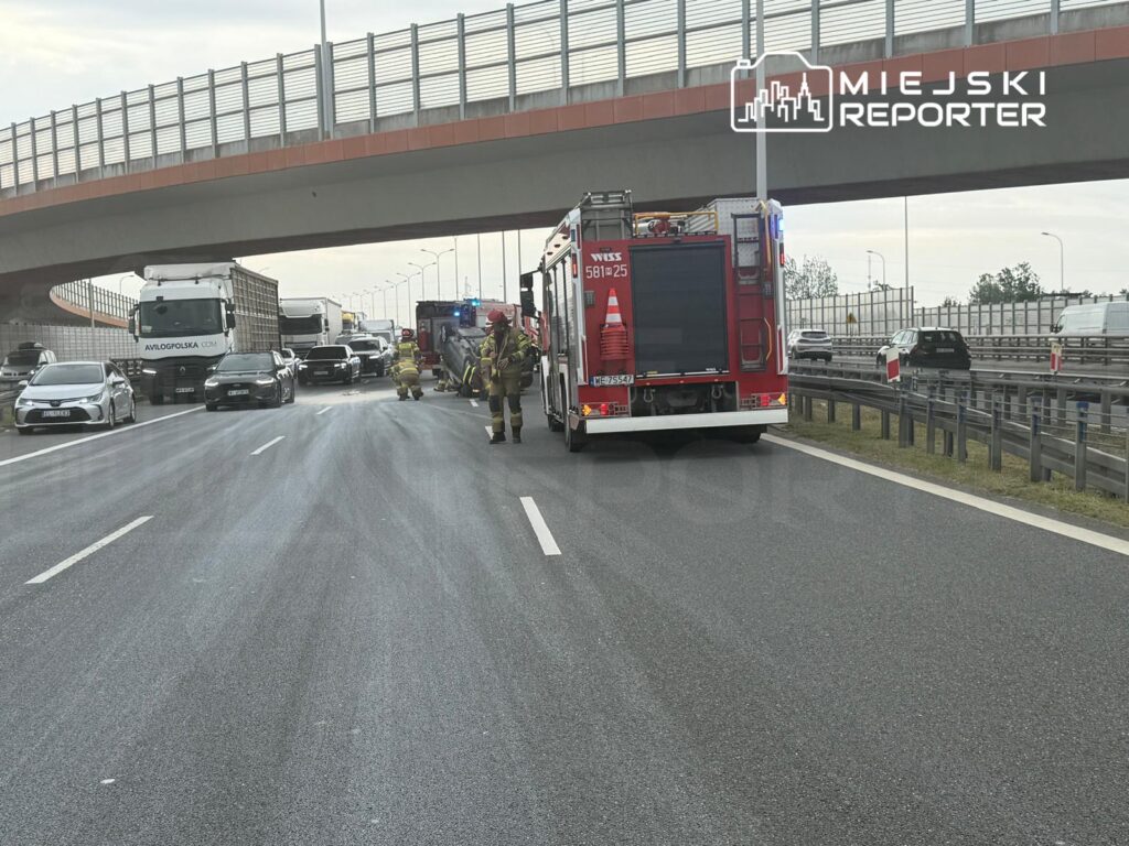 Strażacy pracują nad usunięciem skutków zdarzenia drogowego na autostradzie, obok stojących pojazdów.